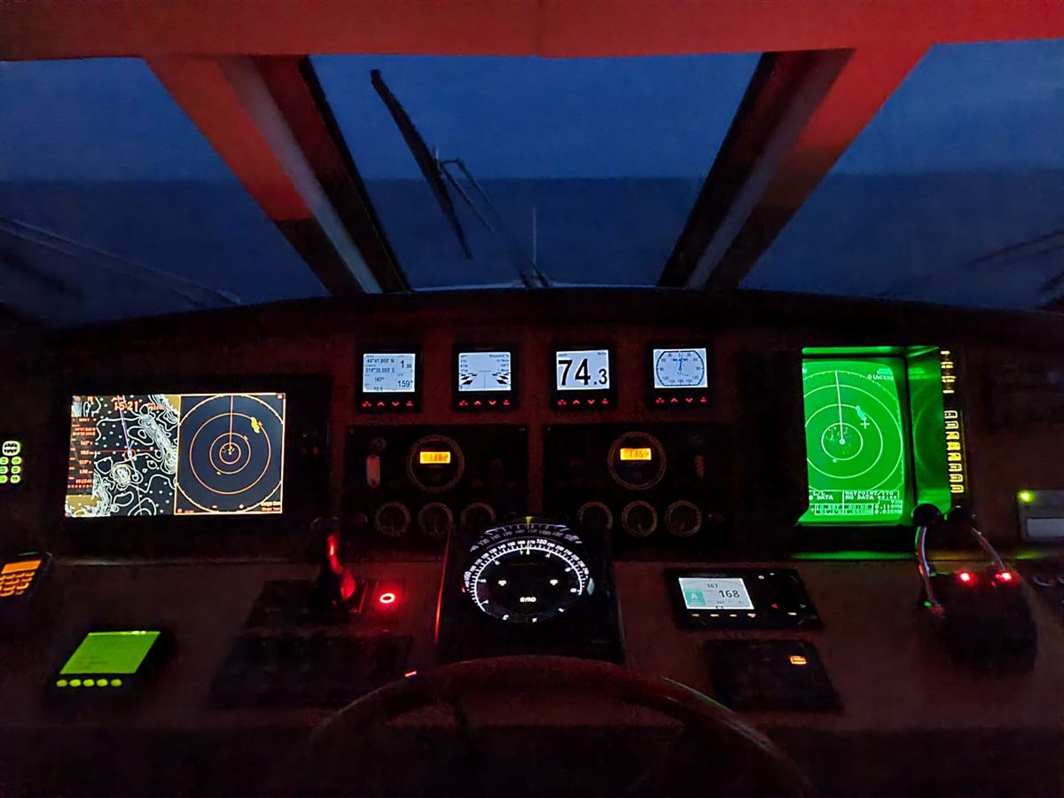 A yacht bridge at dusk with radar and chart displays lit