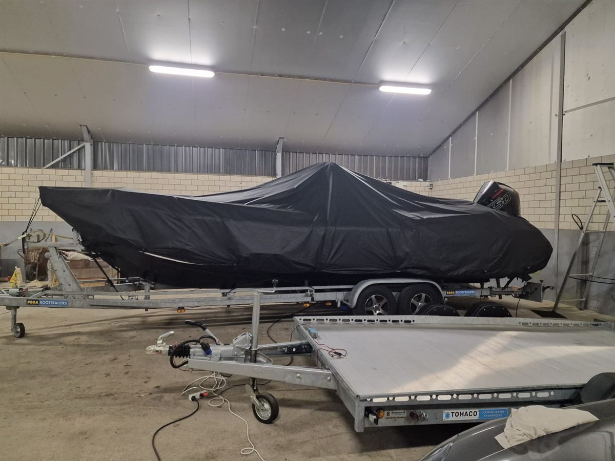A covered motor boat on a trailer, stored in a shed
