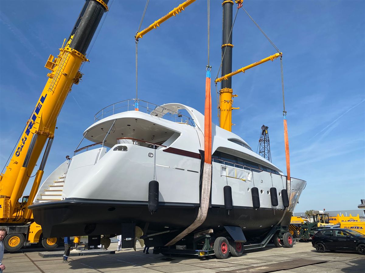 A motor yacht lifted by two mobile cranes in a boatyard