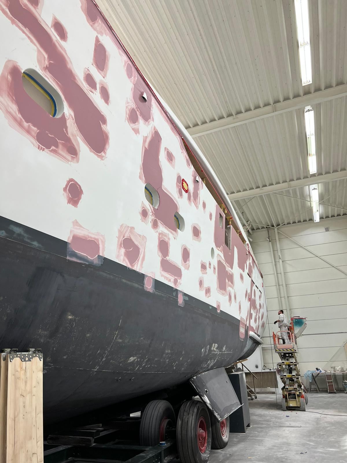 A sailing yacht hull in a shed with areas filled and faired before painting