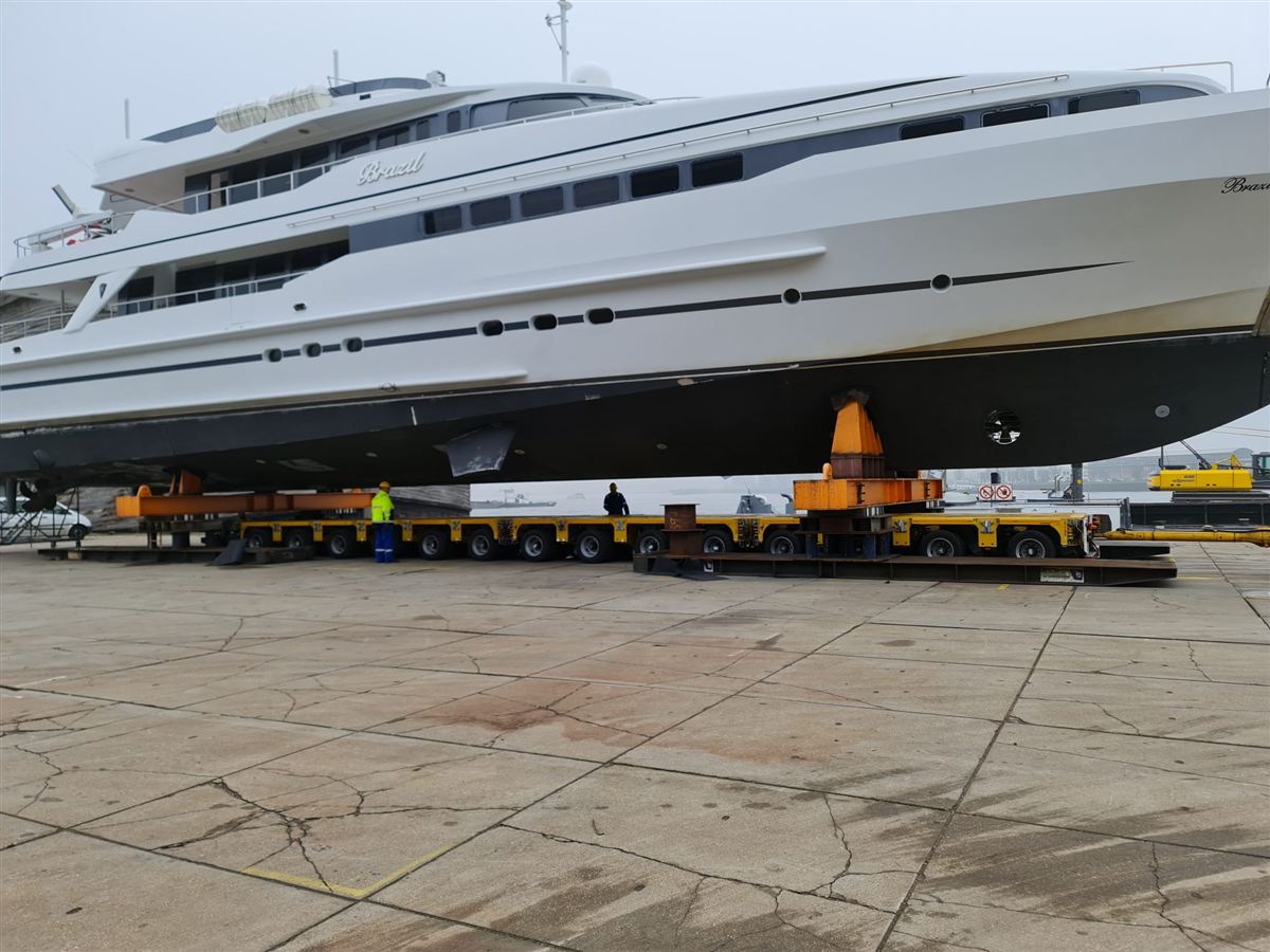 A large motor yacht moved through a shipyard on self-propelled transporters