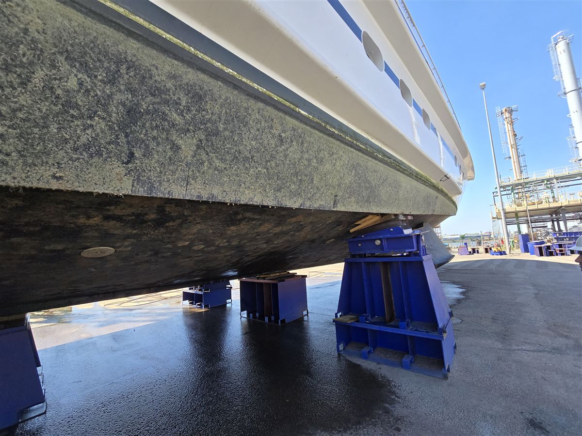 The hull of a large motor yacht below the waterline, supported on blocks