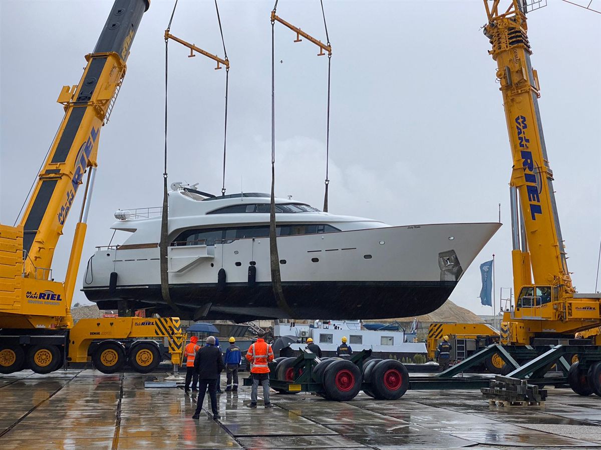 A motor yacht lifted between two mobile cranes onto a transport trailer